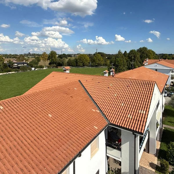 Tetti di case bianchi con tegole arancioni e cielo azzurro, circondati da alberi e prato verde.